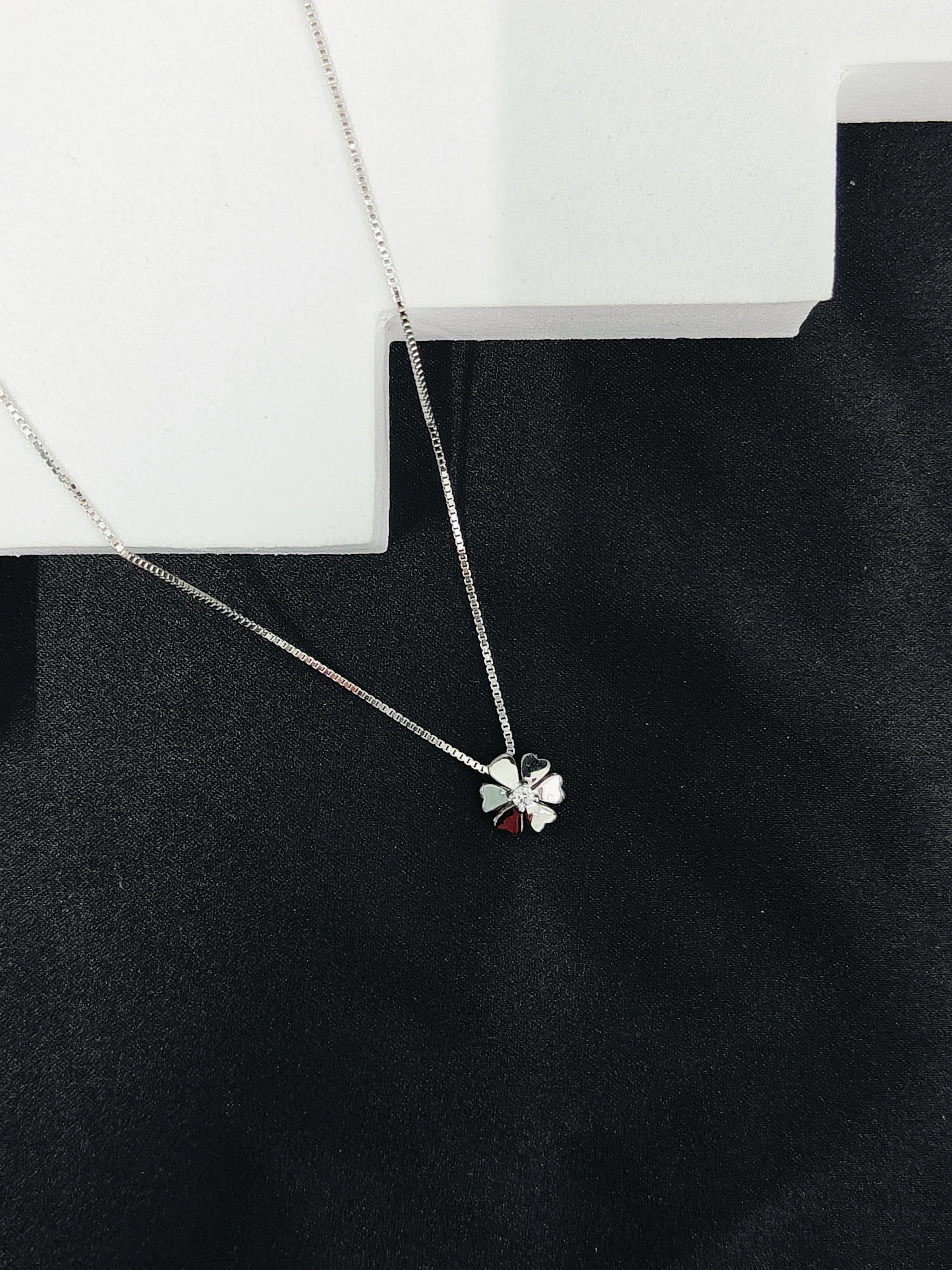 Silver necklace with a clover pendant on a black surface